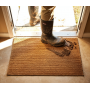 Tapis coco sur mesure 17 mm couleur naturelle posé sur l’entrée, personne en bottes à l’extérieur.