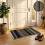 Tapis d’entrée Viva abstract avec rebords 50x70 cm posé devant une porte, motif Stripes noir, beige et blanc; dessous un robot d