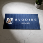 Tapis personnalisé absorb+ sans rebords - 130 x 60 cm affichant le logo “AVODIRE avocats” sur fond bleu, posé sur marbre avec pl