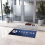 Tapis personnalisé absorb+ sans rebords - 130 x 60 cm bleu foncé posé dans l’entrée devant des portes vitrées.