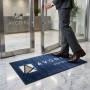 Tapis d'entrée bleu personnalisé absorb+ sans rebords, mesurant 130 x 60 cm, devant des portes vitrées d’immeuble.
