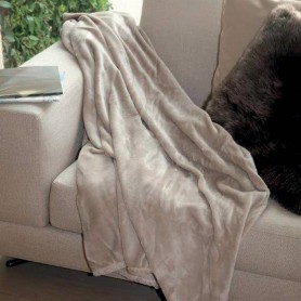 Plaid en microfibre beige posé sur canapé, couverture douce drapée avec coussin noir à côté.