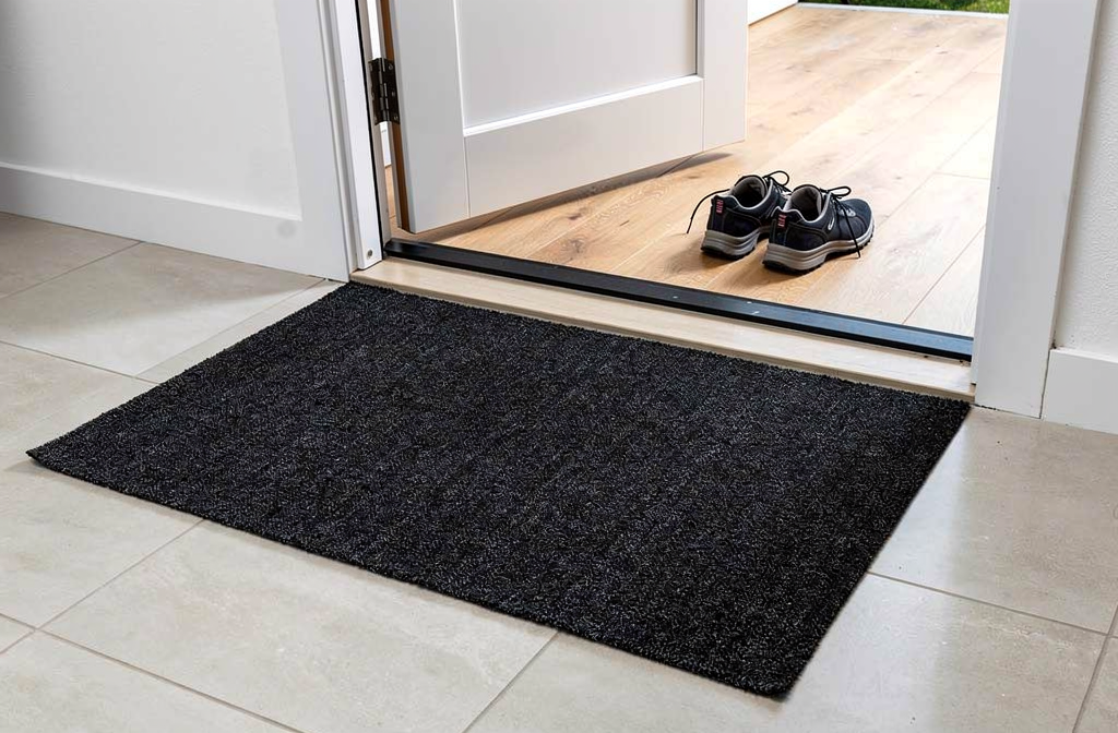Paillasson lavable noir moucheté placé devant une porte d'entrée moderne.