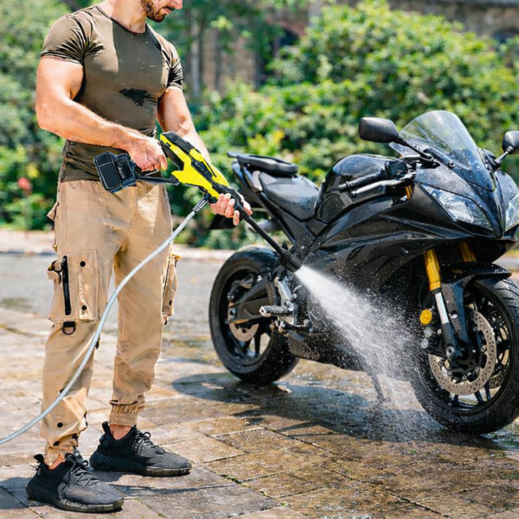 Homme nettoyant une moto noire avec un karcher portable jaune et noir, eau éclaboussant sur la moto et le sol pavé.