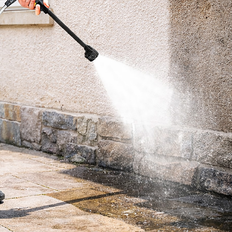 Personne lavant une façade avec un jet d’eau haute pression sur le mur et le sol pavé.