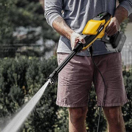 Homme utilisant un nettoyeur haute pression pour tapis d’extérieur, poussant de l’eau sur un tapis en extérieur. comment entretenir un tapis d'extérieur.